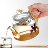 Tea being poured from a decorative glass teapot with floral design into a glass.