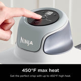 Ninja foodi appliance with digital display and hand pressing a button, set against a neutral background.