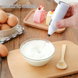 Electric mixer being used to whip cream in a bowl on a wooden table with eggs and a cake in the background.