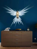 Decorative wall art of a bird with wings spread on a blue wall above a wooden cabinet.