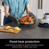 Person holding a glass dish with roasted chicken on a kitchen counter, wearing heat-resistant gloves.